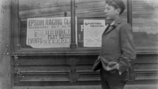 A boy, Francis Bane, stands in front of a poster advertising the Epsom Racing Club. Picture: Joseph Bane, State Library of Victoria