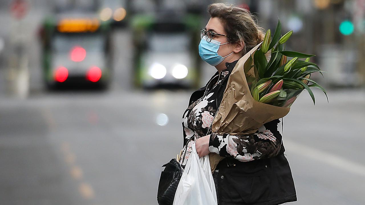 A woman wears a mask while crossing a street in Melbourne. Picture: NCA NewsWire / Ian Currie