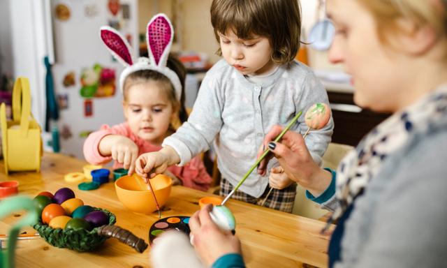 Caring single mother helping  to her daughters to paint an Ester egg with watercolors paint