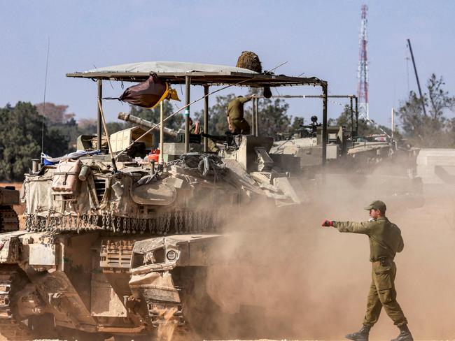 An Israeli army soldier gestures behind a moving main battle tank as forces gather at a position near the border with the Gaza Strip in southern Israel. Picture: AFP