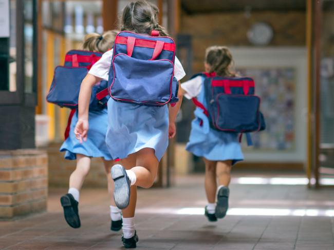 Rear view of excited students running towards entrance. Girls are carrying backpacks while leaving from school. Happy friends are wearing school uniforms. Source: iStock