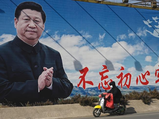 A man rides a scooter past a billboard showing Chinese President Xi Jinping with a slogan which reads "Remain true to our original aspiration and keep our mission firmly in mind" in Beijing on February 28, 2023. (Photo by Jade Gao / AFP)