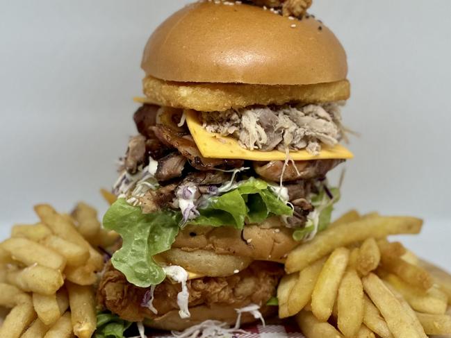 The Mega Boom Burger has chicken, double pulled pork, double beef brisket, crispy bacon, cheese, lettuce, onion rings, slaw, barbecue sauce, mayonnaise and topped with onion rings and a chicken ring.