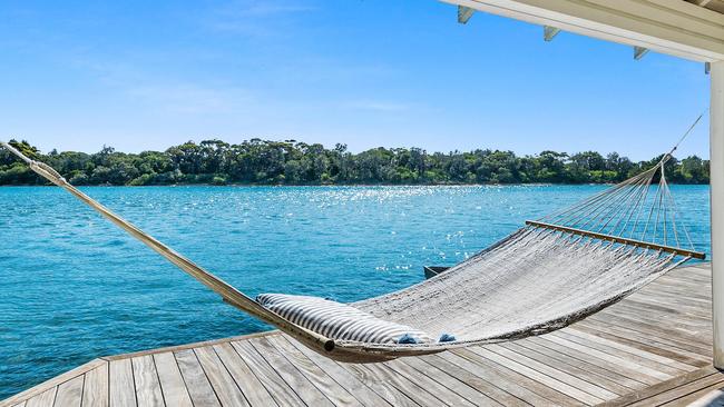 The home has expansive teak decks, manicured gardens, and a private boatshed that extends into the water.