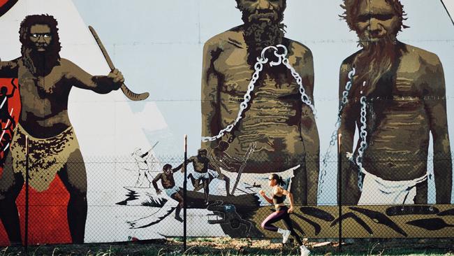 Cathy Freeman runs past a giant mural in Melbourne’s Northcote of Aboriginal elders in chains before the 1994 Commonwealth Games. Picture: Wayne Ludbey