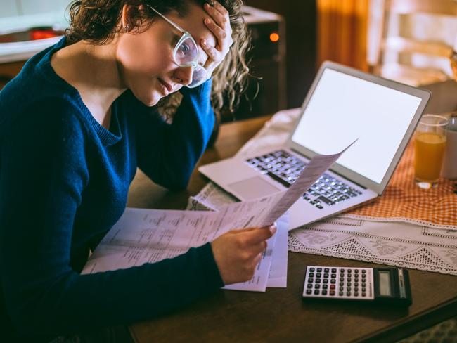 Young female reading documents, using calculator and laptop in the kitchen at home