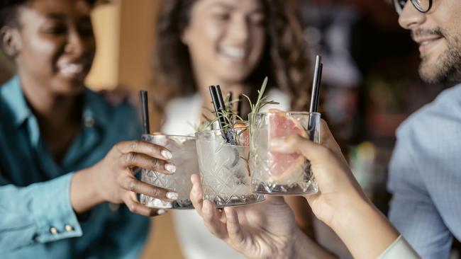 People with alcohol drinks clinking glasses in a restaurant having fun together, laughing, drinking cocktails. Party, celebration, nightlife and people concept - smiling friends clinking glasses