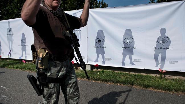 A gun rights advocate carries an assault style rifle past a poster depicting the victims of the Sandy Hook Elementary School mass shooting in 2017. Picture: Brendan Smialowski/AFP