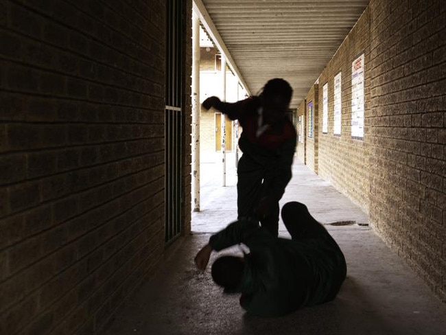 Two school kids fight in a dark passageway of their school, almost silhouette.