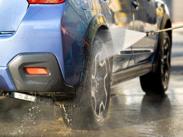 Closeup of male driver washing his car with contactless high pressure water jet in self service car wash.