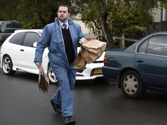 An officer carries a large number of paper evidence bags from the crime scene.