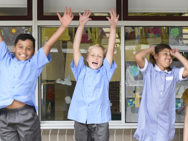 Excited school children with arms in the air and proud school teacher smiling