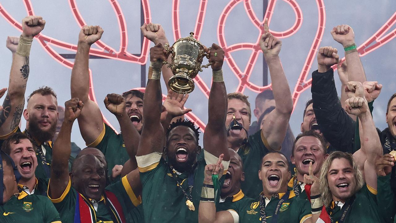 South Africa's flanker and captain Siya Kolisi (CR) lifts the Webb Ellis Cup on the podium as he stands next to President of South Africa Cyril Ramaphosa (CL) after South Africa won the France 2023 Rugby World Cup Final match between New Zealand and South Africa at the Stade de France in Saint-Denis, on the outskirts of Paris, on October 28, 2023. (Photo by Anne-Christine POUJOULAT / AFP)