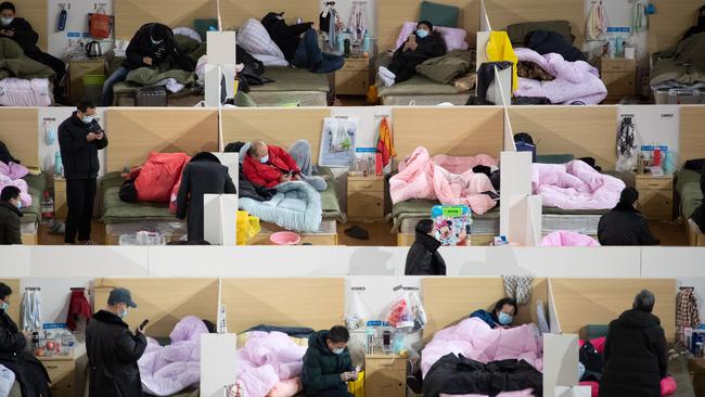 Medical personnel walk among patients with mild symptoms of the COVID-19 coronavirus resting at night in the temporary hospital set up in a sports stadium in Wuhan in February as the virus ran riot. Picture: AFP