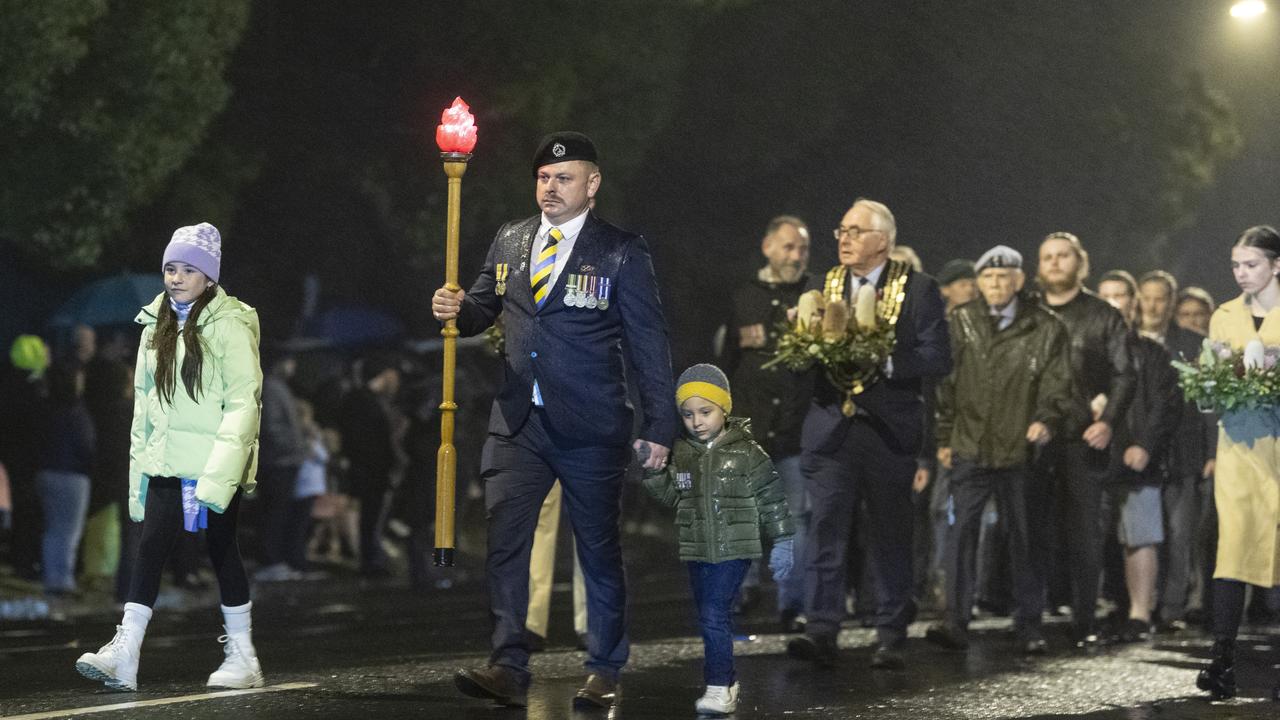 The Torch is carried along Margaret St in the pre-dawn by Joshua Hawkins with kids Arianna Riwoe and Harlin Hawkins on the march to the Anzac Day Toowoomba Dawn Service, Tuesday, April 25, 2023. Picture: Kevin Farmer