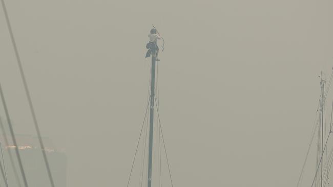 A crew member climbs the mast of a yacht docked at the Cruising Yacht Club of Australia as smoke covers the city and forces the cancellation of the Grinders Coffee SOLAS Big Boat Challenge on Sydney Harbour. Picture: Brett Costello