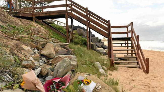 The Dicky Beach surfing community is reeling after the body of a young woman washed ashore. Flowers have been left at the botom of the staircase in her remembrance.