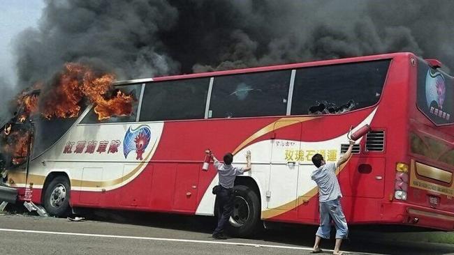 A policeman and another man try to break the windows of a burning tour bus on the side of a highway in Taoyuan, Taiwan. Picture: Yan Cheng/Scoop Commune via AP