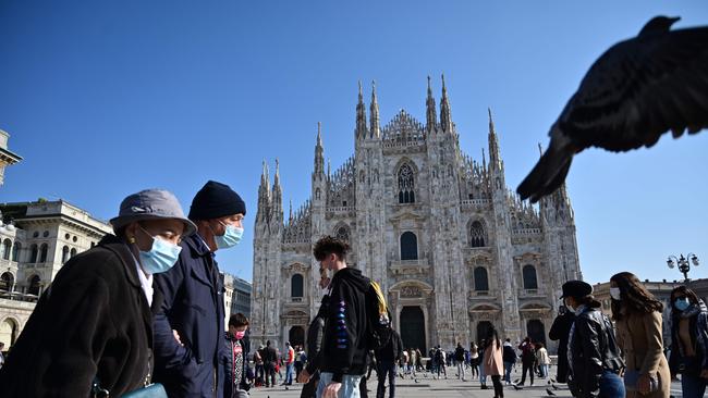 People wearing protective masks walk across the Piazza del Duomo in Milan, Italy. The government has made it mandatory for masks to be worn outdoors. Picture: AFP