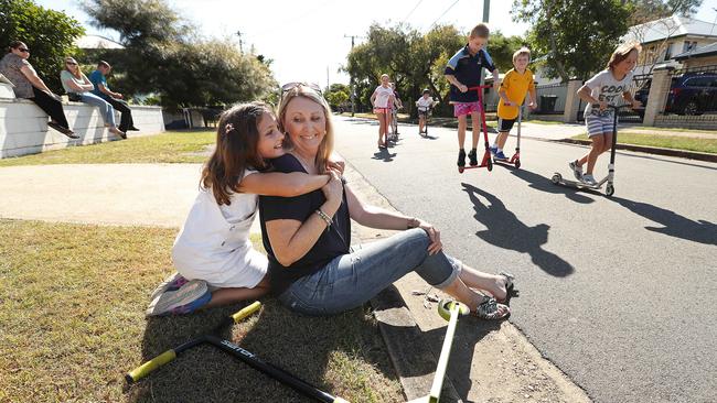 With a cuddle from twin daughter Evie Turner 8, Liz Campbell watches her other twin Campbell Turner play with neighbourhood friends in the Brisbane suburb of Nundah. Picture: Lyndon Mechielsen