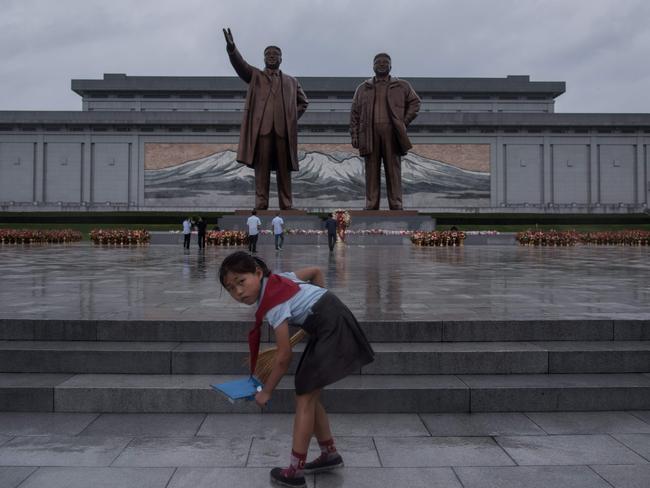 A young girl cleans steps as people bow before the statues of late North Korean leaders Kim Il-sung, left, and Kim Jong-il as the country marks 'Victory Day' at Mansu hill in Pyongyang on July 27, 2017. Picture: AFP