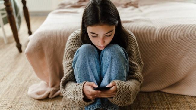 Teenage girl sitting on the floor and scrolling a smartphone.