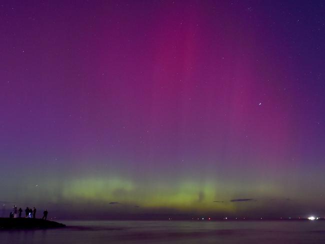 People watch the the aurora australis or southern lights caused by a solar storm at Port Phillip Bay in Melbourne on May 11, 2024. (Photo by Paul CROCK / AFP)