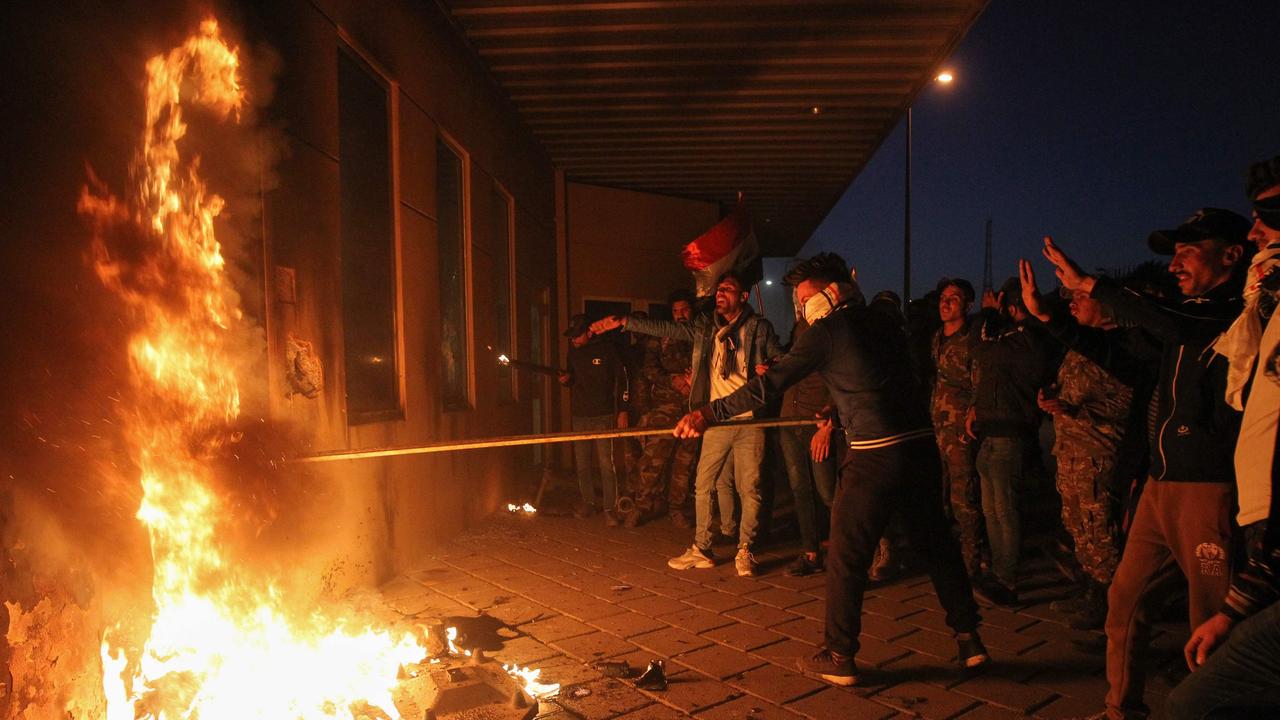 Members of Iraq’s Hashed al-Shaabi military network set a door ablaze as they try to break into the US Embassy. Picture: Ahmad Al-Rubaye/AFP