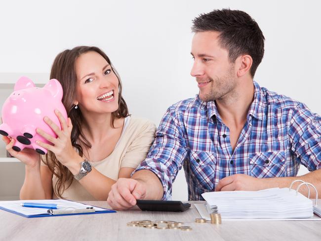 Young Man Looking At Woman Inserting Coin In Piggybank