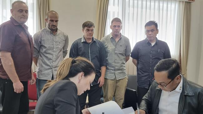 Indonesian and Australian officials sign handover documents as five Australians who have spent almost 20 years in Indonesian prisons for heroin trafficking look on, prior to their return to Australia, in Bali, Indonesia. Picture: Supplied/Indonesian Coordinating Ministry for Legal, Human Rights, Immigration and Correctional Affairs via AP