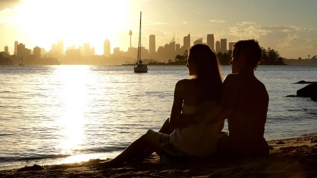 At Milk Beach, a young couple take in the view of the city skyline across Sydney Harbour at sunset.