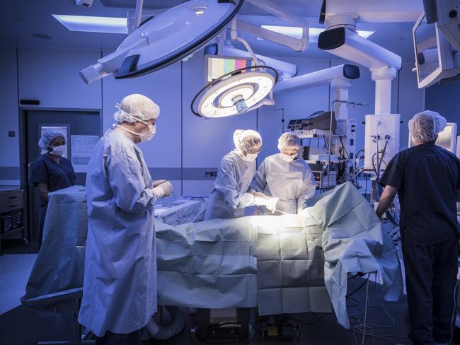 Four doctors in hospital operating room with patient lying on operating table. Surgical lights shining on medical team performing operation on patient