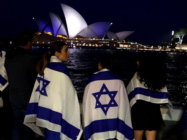 People with Israeli flags watch the Opera House while it is illuminated in blue to show solidarity with Israel in Sydney on October 9, 2023. Israel relentlessly pounded the Gaza Strip overnight and into October 9 as fighting with Hamas continued around the Gaza Strip, as the death toll from the war against the Palestinian militants surged above 1,100. (Photo by David GRAY / AFP)