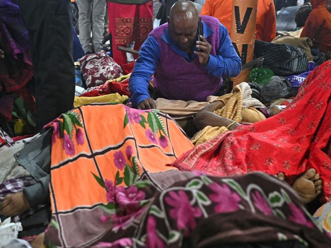 A devotee speaks on a mobile phone while sitting beside the victims at the site of a stampede. Picture: AFP