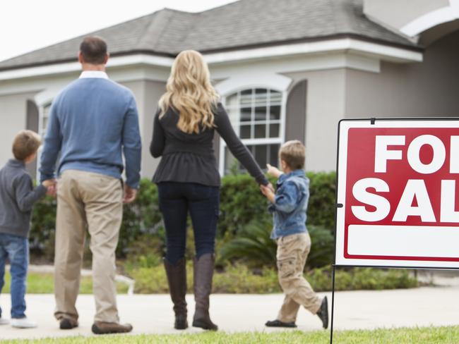 Family with two boys (4 and 6 years) standing in front of house with FOR SALE sign in front yard.  Focus on sign.