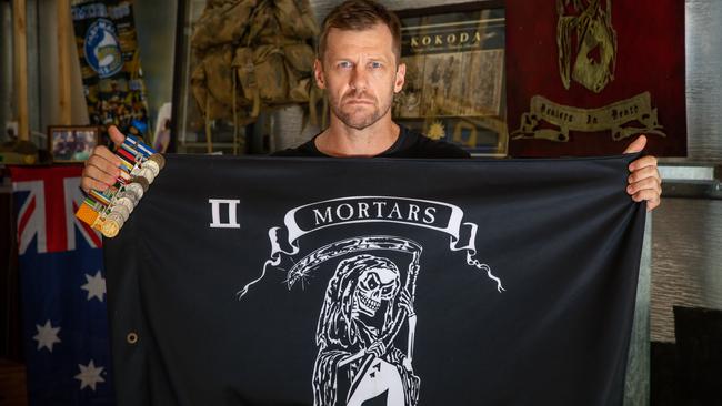 Afghanistan veteran Justin Huggett at his Townsville home with his medals and a mortar platoon flag bearing the motto ‘Dealers in Death’. Picture:  Cameron Laird