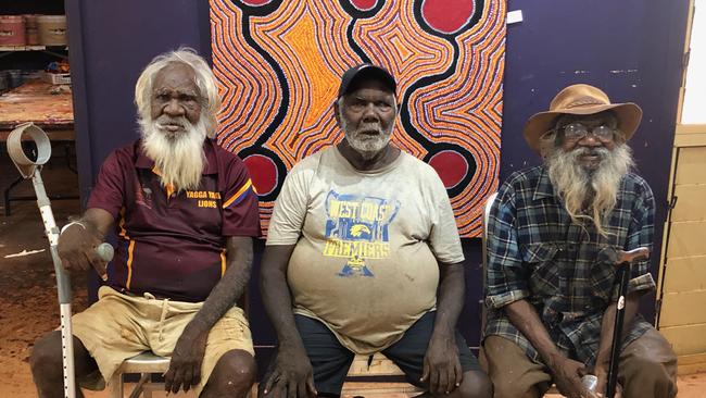 Balgo-based artists, from left, Larry Gundora, Jimmy Tchooga and Helicopter Tjungurrayi in the Tanami Desert. The painting behind is artwork by Jimmy Tchooga.