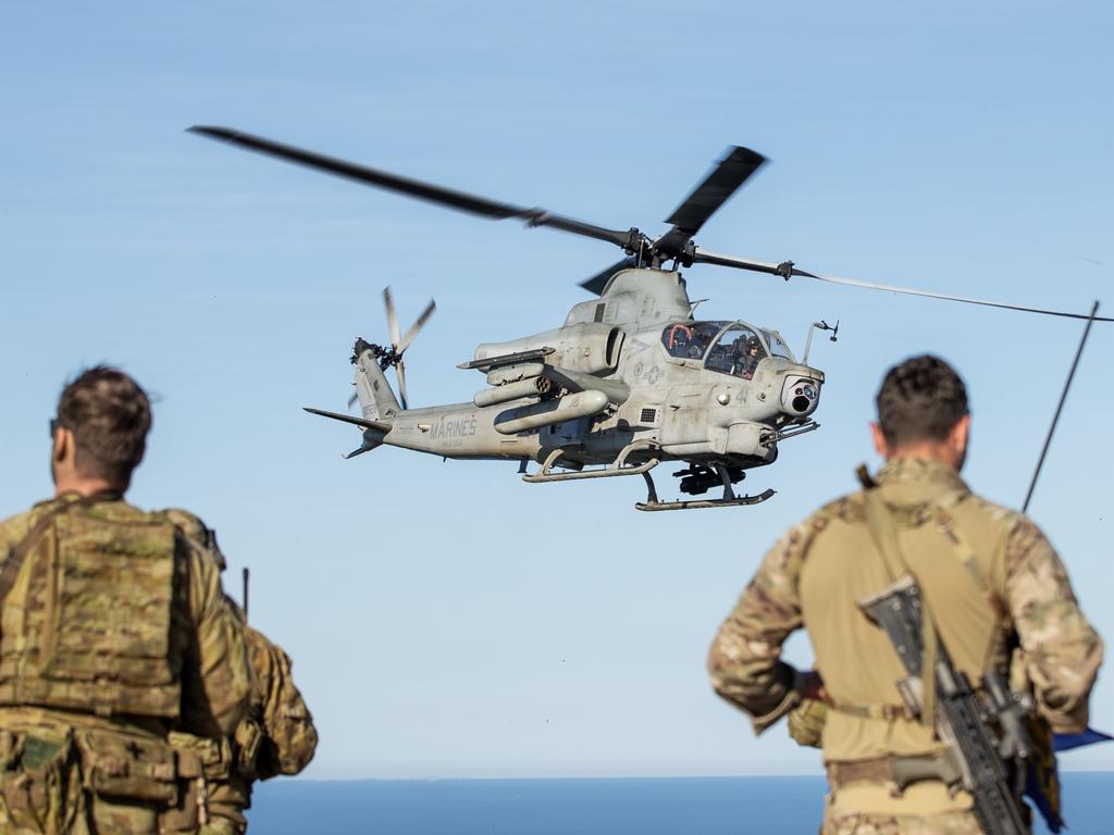 Australian Army soldiers and British Royal Marine Commandos stand at an observation post on Townshend Island while a United States Marine Corps Bell AH-1Z Cobra hovers behind them.