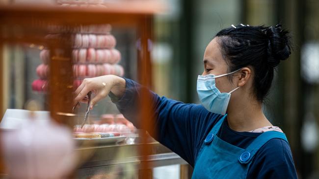 MELBOURNE, AUSTRALIA - DECEMBER 24: A hospitality worker wear a face mask as she works at Royal Arcade Gallery on December 24, 2021 in Melbourne, Australia. Victoria has reintroduced rules for masks to be worn in indoor settings, as COVID-19 case numbers continue to rise.  From 11:59pm on Thursday 23 December, all Victorians aged 8 and up are required to wear a mask in all non-residential indoor settings. Masks must also be worn while moving around at major events attracting at least 30,000 people, but can be taken off by patrons while sitting down. (Photo by Diego Fedele/Getty Images)