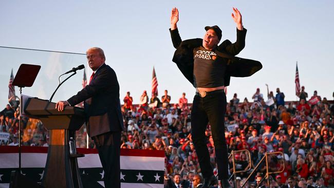 Tesla CEO Elon Musk (R) jumps on stage as he joins former US President and Republican presidential candidate Donald Trump during a campaign rally. Photo by Jim WATSON / AFP