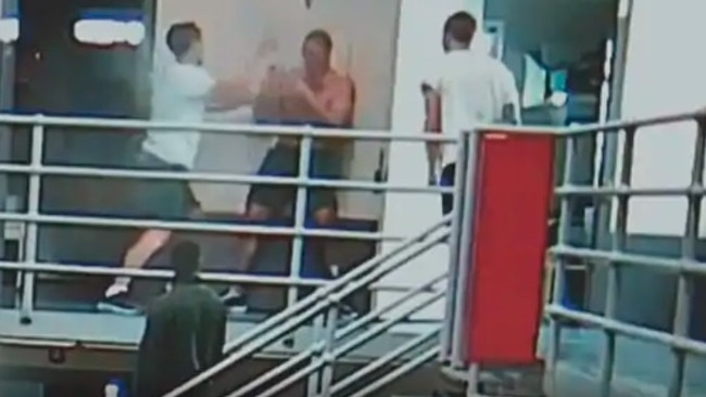 Two inmates in white tshirts approach a shirtless fellow inmate.