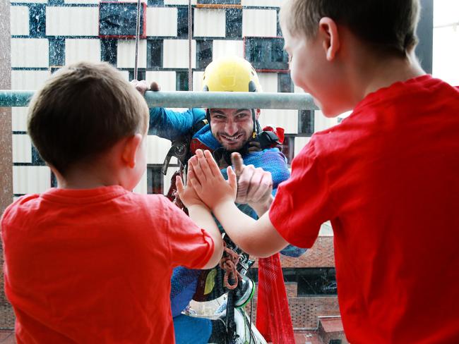 Brothers Ben, 7, and Morgan Walder, 3, trade high-fives through the glass with Superman as he abseils down the Lady Cilento Children's Hospital. Picture: Claudia Baxter