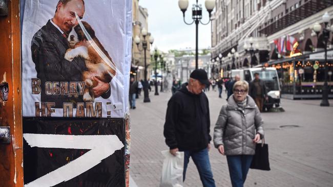 People walk past a gift shop in central Moscow next to T-shirts bearing the letter Z, a tactical insignia of Russian troops in Ukraine, and a picture of Vladimir Putin cuddling a dog. Picture: AFP.