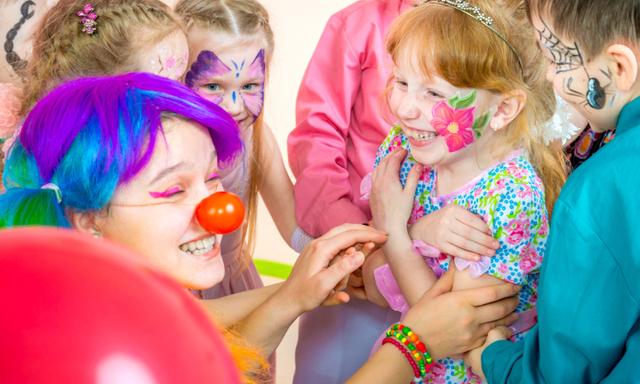 The group of well-dressed children of preschool and elementary age are having fun at birthday party. Cheerful female clown is entertaining the kids at a children's party. Children and clown are congratulating the little birthday girl. They are tickling the little girl together. Studio shooting