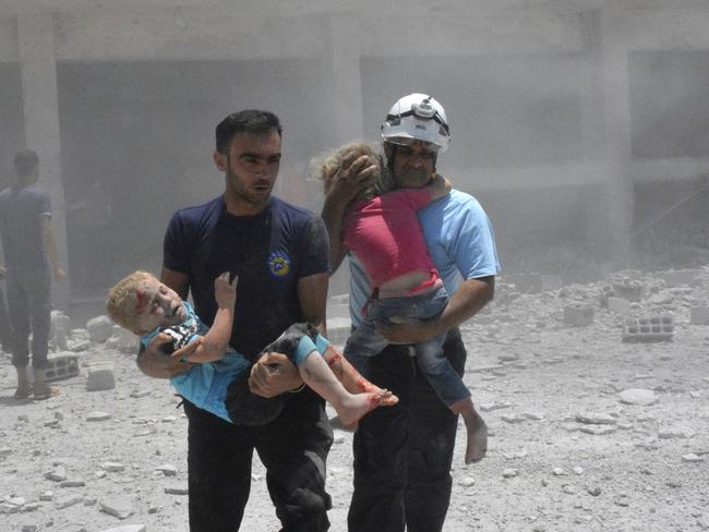 White Helmets carry children after air strikes hit a school housing a number of displaced people. Picture: Syrian Civil Defense White Helmets via AP