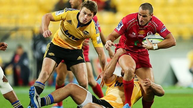 Mike Harris is held by Hurricanes defender as Beauden Barrett looms up to finish off the tackle.