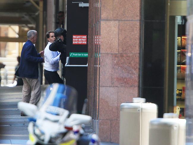 Two of the hostages escape the cafe yesterday while a police officer keeps his gun aimed at the cafe. Picture: Toby Zerna