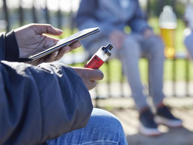 Close Up Of Teenagers With Mobile Phone Vaping and Drinking Alcohol In Park