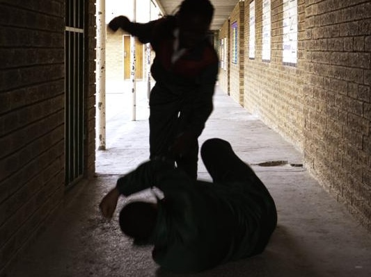 Two school kids fight in a dark passageway of their school, almost silhouette.