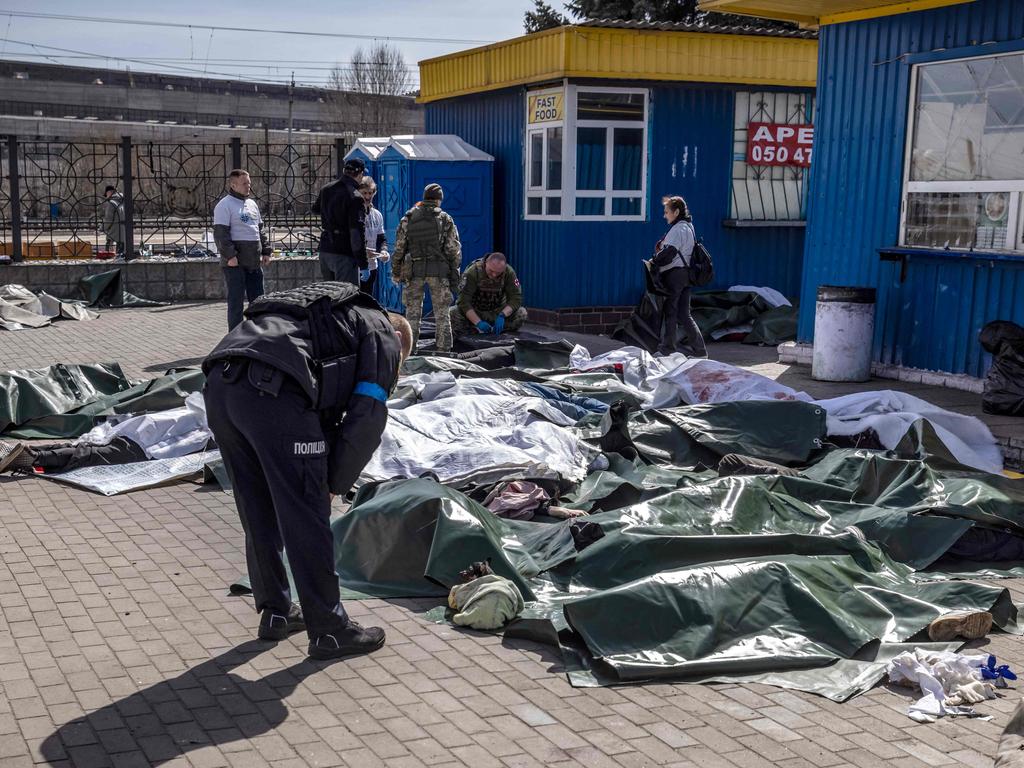 A Ukrainian policeman bends over bodies laid on the ground and covered with tarpaulin after a rocket attack at a train station in Kramatorsk. Picture: AFP